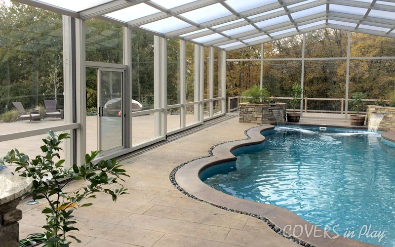 Side angle view of residential pool dome enclosure with slidine door and waterfall